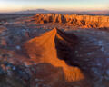 A sunlit desert ridge casts a dramatic shadow beneath Utah’s towering cliffs and distant mountains.