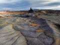A lone desert butte rises beneath stormy skies with distant snow-capped mountains beyond.