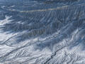 Blue-gray Utah badlands ripple gently in a minimalist aerial study of erosion and light.
