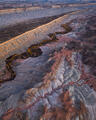 Winding river with golden cottonwoods through layered Utah badlands beneath a long escarpment.