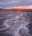 Gray Utah badlands with branching desert washes beneath red sunset mesas.