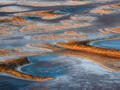 An aerial abstract of glowing island formations and blue pools across an Australian dried lake bed.
