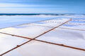 An aerial view of geometric salt ponds and reflective water under soft blue skies in Australia.