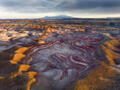 Swirling mineral layers and golden light define Utah’s painted badlands beneath distant mountain peaks