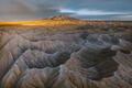 Gray Utah badlands with distant mountains under dramatic golden storm light.