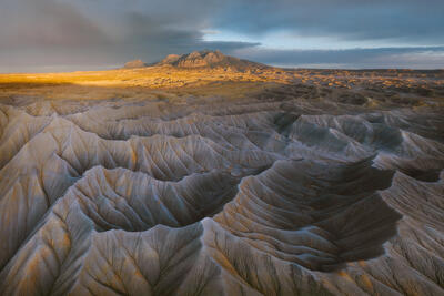 Gray Utah badlands with distant mountains under dramatic golden storm light.