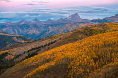 Mountain skyline is pictured with yellow hillsides of aspen trees and a late evening sunset sky.