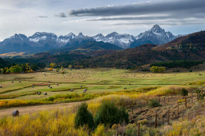 Mountain range in the distance with a field of hay bales and early fall colors of yellow start to show below.