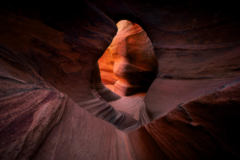 A natural sandstone portal frames the glowing interior of a secluded slot canyon in the American Southwest.