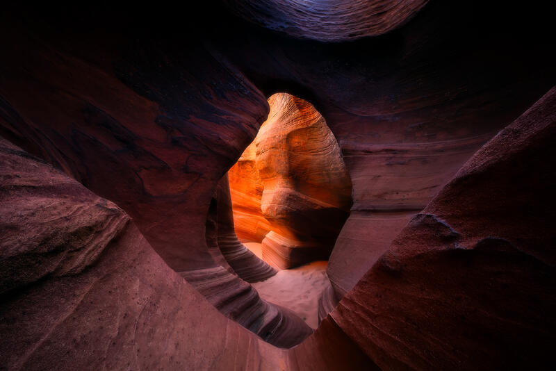 A natural sandstone portal frames the glowing interior of a secluded slot canyon in the American Southwest.