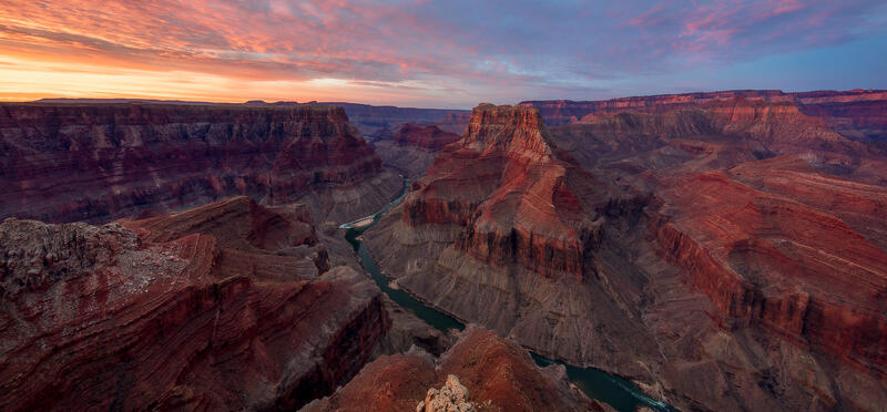 A canyon with striations resembling a marble where the rock layers are visible, with rivers at the bottom  at sunrise.