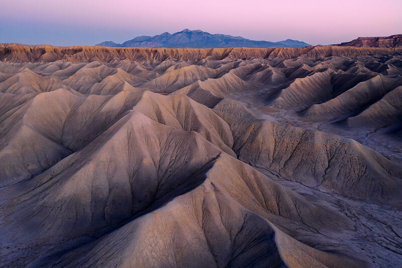 Twilight light washes over Utah’s rolling badlands beneath a distant mountain horizon.