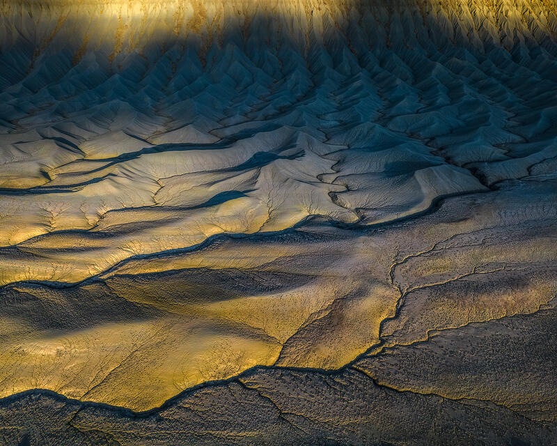 Golden sunrise light traces flowing Utah badland ridges against cool shadowed valleys.
