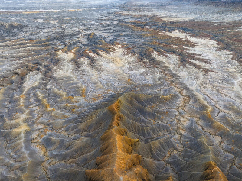 A golden Utah ridge rises like a crown above vast pale badlands.
