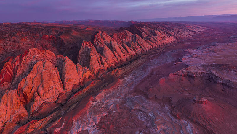 Crimson sandstone cliffs blaze at sunset along a sweeping Utah escarpment on the Colorado Plateau.