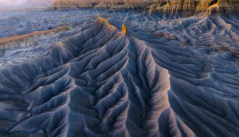 Sunlit sandstone spire rising above blue-gray badlands ridges in Utah.