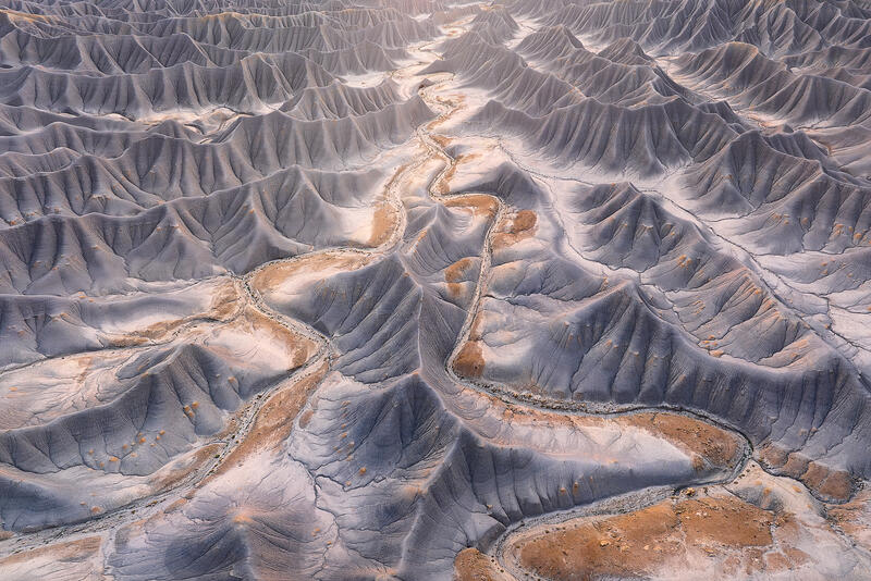 Winding desert wash through pale gray Utah badlands hills.