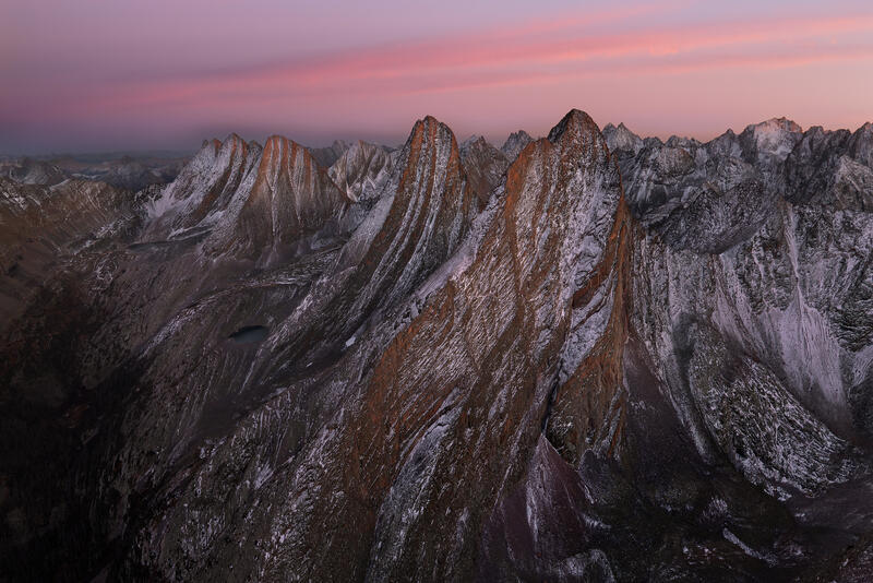 Alpenglow softly illuminates jagged Colorado peaks beneath a pastel dawn sky.