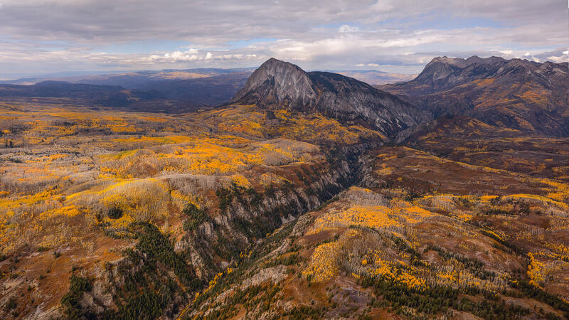 Golden aspen hills surround a rugged granite peak in a sweeping Colorado autumn panorama.