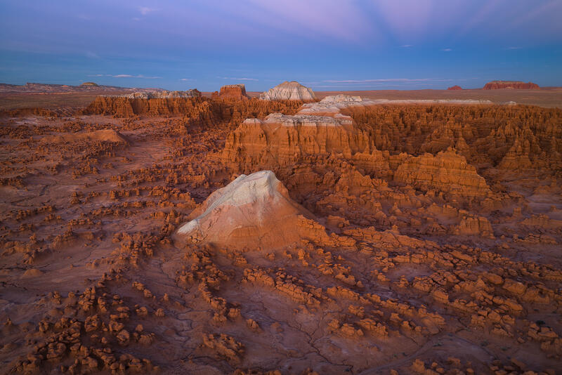 Sunlit red hoodoos and sandstone spires glow beneath soft twilight skies in Utah’s canyon country.