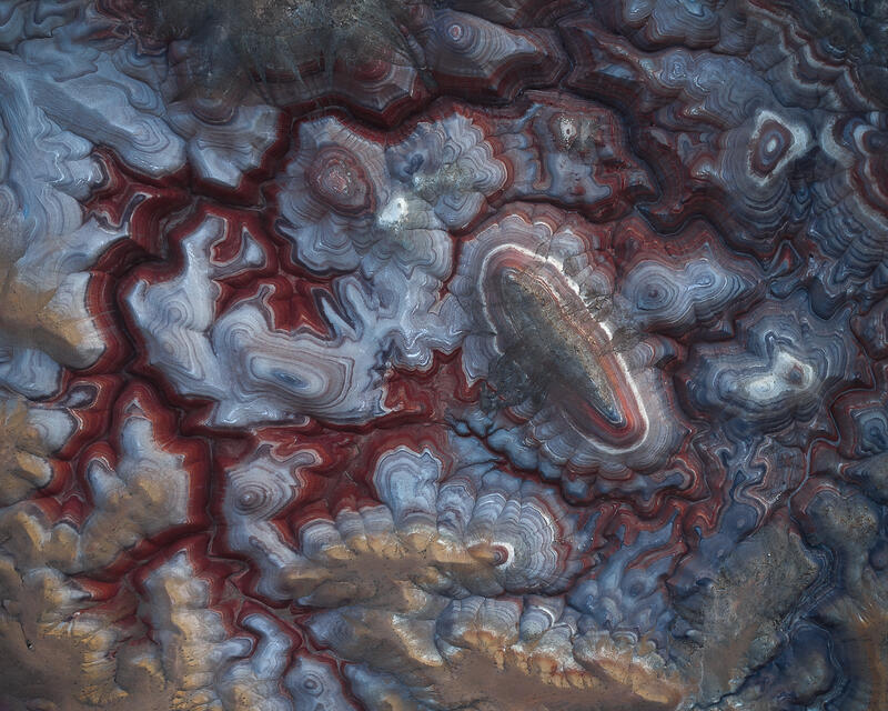 Aerial view of red, blue, and white mineral patterns in Utah badlands.