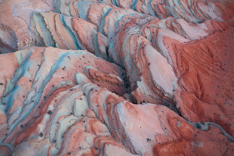 Coral and turquoise mineral bands fold across Utah’s sculpted badlands in a striking aerial abstract.