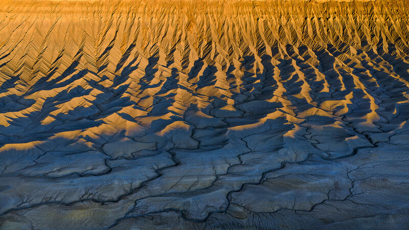 Golden sunset light over Utah badlands with blue shadowed shale ridges.