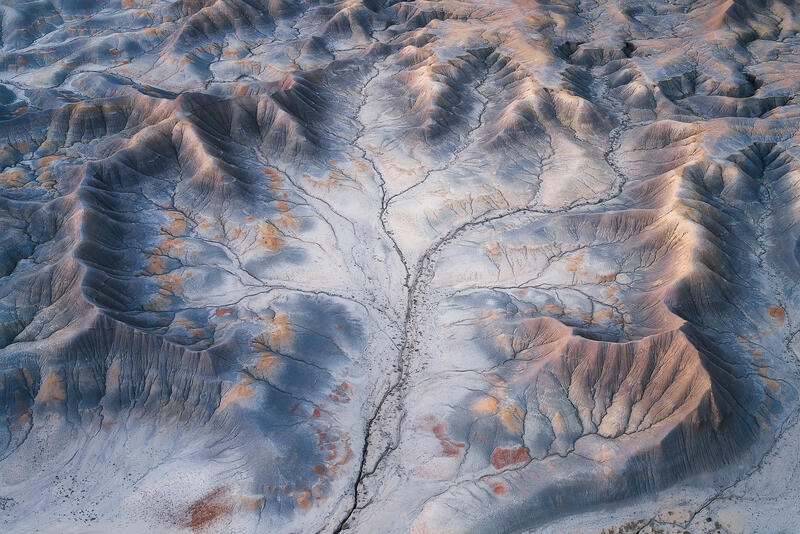 Gray Utah badlands with red mineral patches and branching erosion channels.