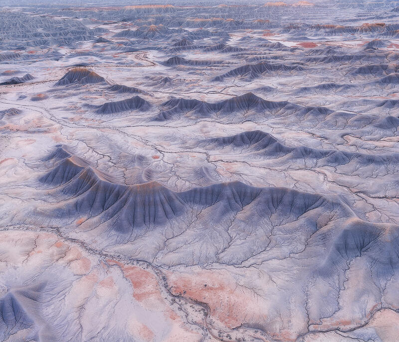 Wide aerial view of pale blue Utah badlands basin with repeating ridges.