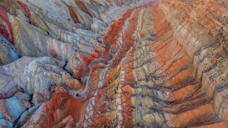 Colorful bands of red, blue, and cream ripple through Utah’s badlands in an abstract aerial view.