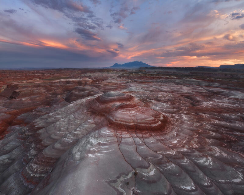 A glowing sunset sky rises above layered badlands and distant mountains in Utah.