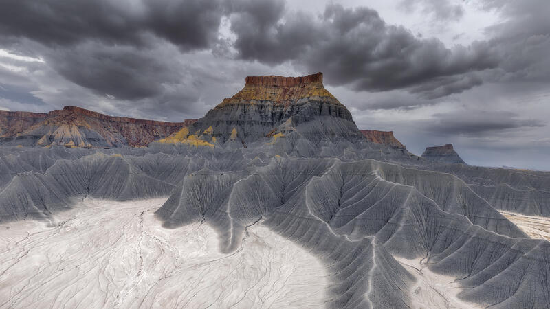 Storm clouds loom over Factory Butte as gray badlands ripple across Utah’s desert in dramatic light.