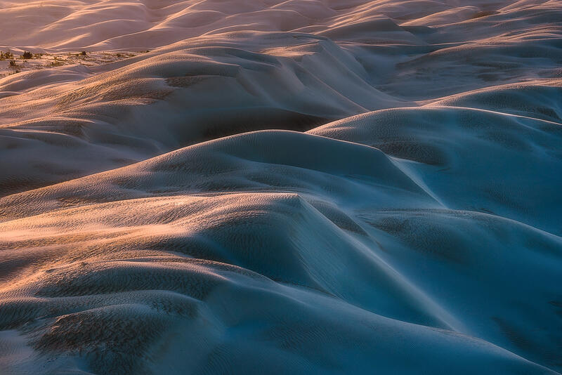 An elegant aerial view of rolling sand dunes shaped into soft abstract forms by wind and light.