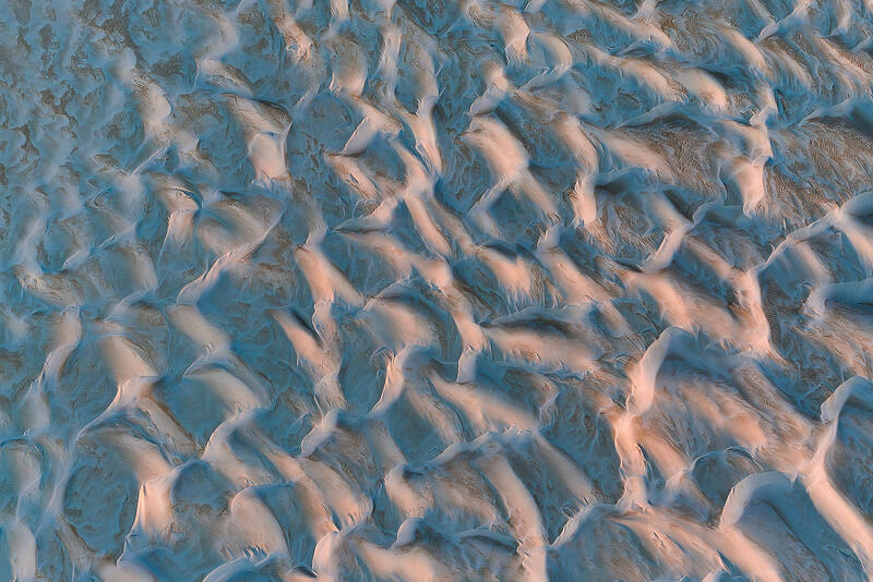 An abstract aerial study of Australian sand dunes shaped into flowing textures by light and wind.