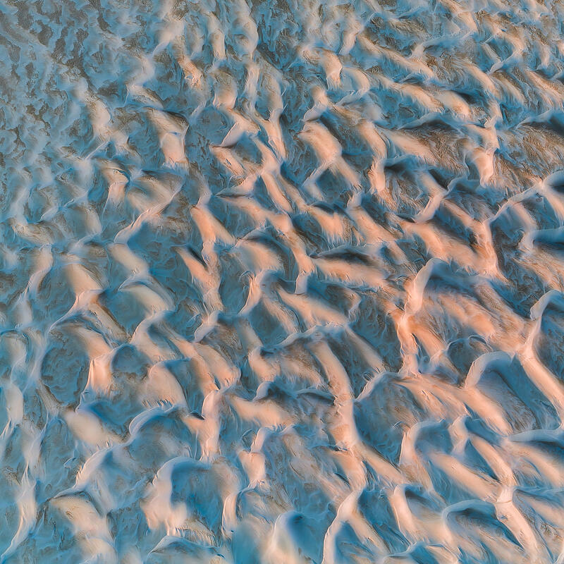 An abstract aerial of rolling Australian sand dunes shaped by light, wind, and shadow.
