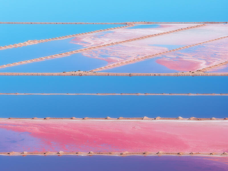 Pastel salt ponds and reflective blue water form a playful aerial abstract across the Australian landscape.
