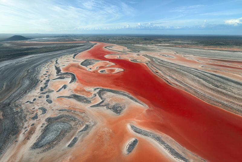 An aerial view of a brilliant red waterway flowing across an Australian salt and desert landscape.
