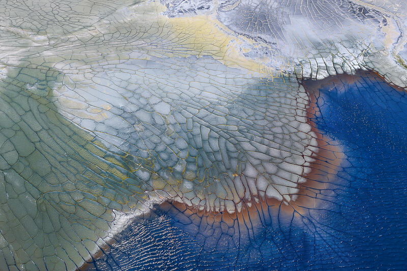 An abstract aerial of cracked mineral flats surrounding deep blue water in the Australian landscape.