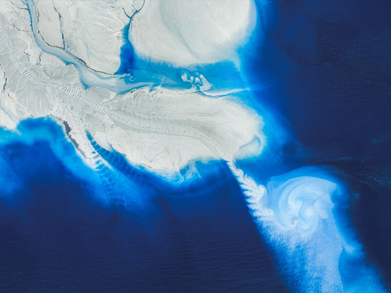 An aerial abstract of bright blue water and white mineral formations along an Australian salt shoreline.