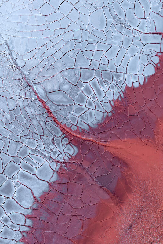 An abstract aerial of cracked white and red mineral surfaces across an Australian dried lake bed.

