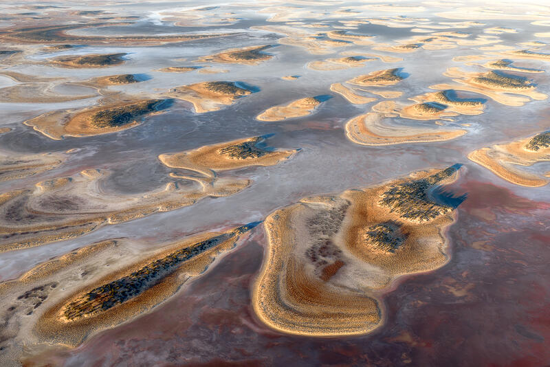 An aerial view of island-shaped formations across a dried Australian lake bed at golden hour.