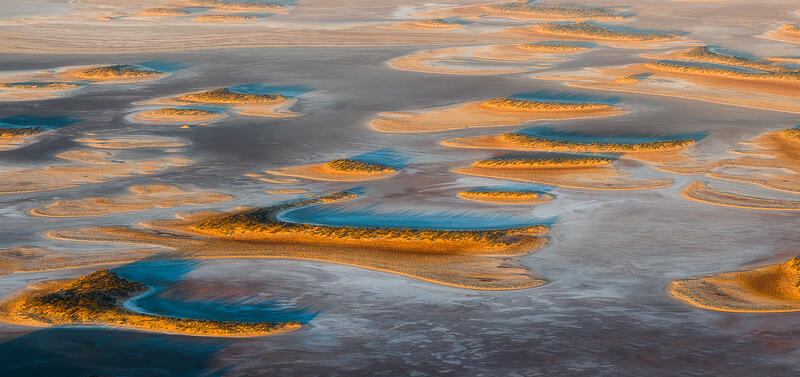 An abstract aerial of island-like formations scattered across a textured dried lake bed in the Australian outback.