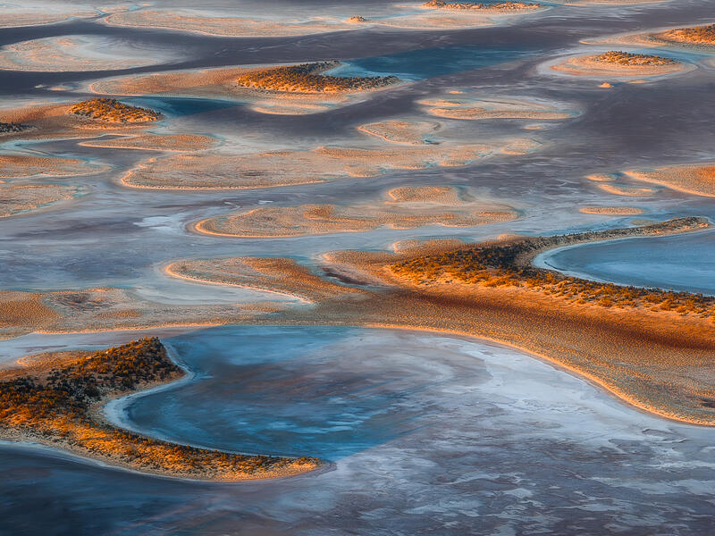 An aerial abstract of glowing island formations and blue pools across an Australian dried lake bed.
