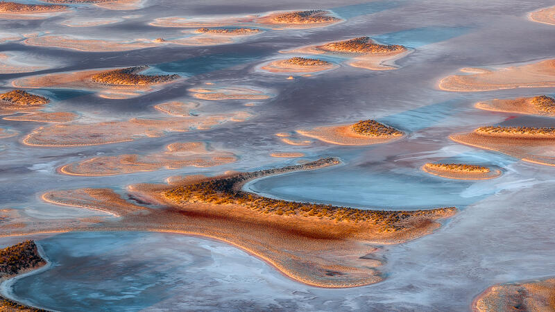 An abstract aerial view of isolated landforms scattered across a dry Australian lake bed in soft natural color.