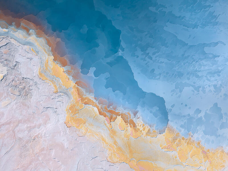 An abstract aerial of pastel mineral edges and flowing blue textures across an Australian salt landscape.
