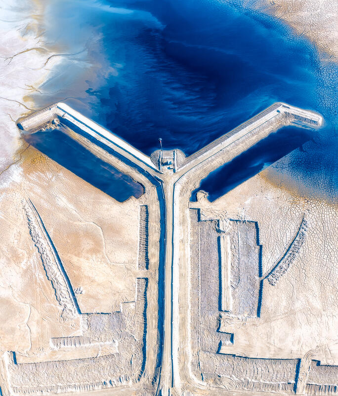 A geometric network of roads and vivid blue water forms a striking abstract aerial pattern across pale salt flats.