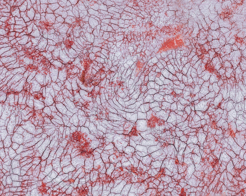 An aerial abstract of delicate red fracture patterns across pale mineral surfaces in Australia.