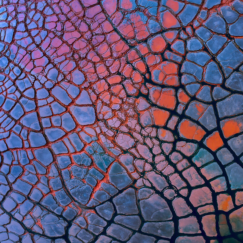 An abstract aerial of colorful cracked earth patterns forming a vibrant natural mosaic.