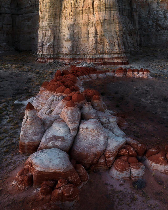 Red and white Utah hoodoos beneath a massive layered sandstone cliff.