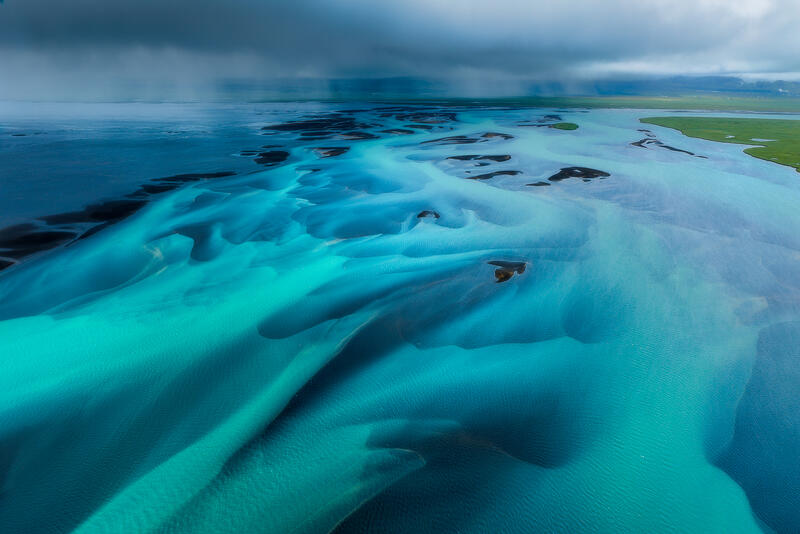 Turquoise glacial rivers sweep toward Iceland's coast in a luminous aerial abstract.